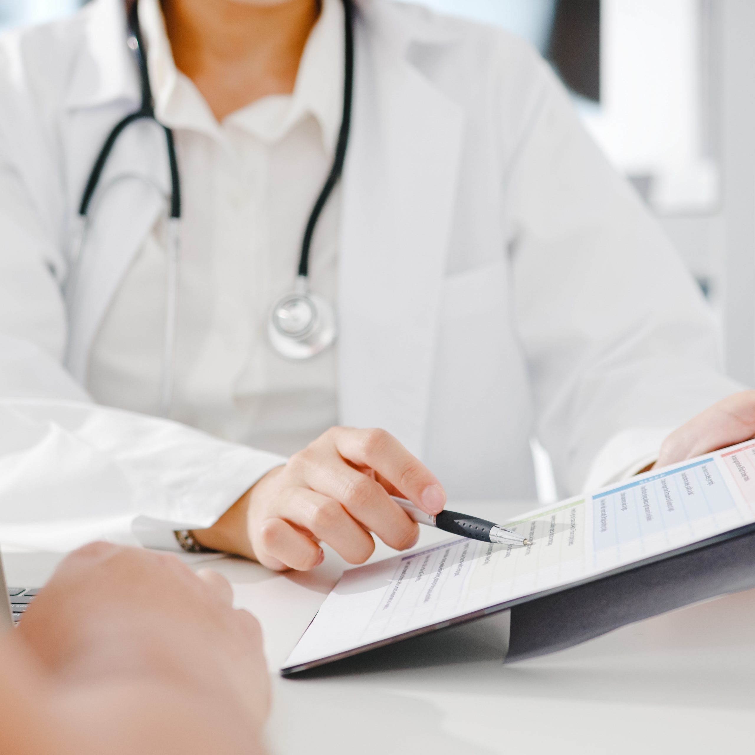 Young Asia female doctor in white medical uniform using clipboard is delivering great news talk discuss results or symptoms with male patient sitting at desk in health clinic or hospital office.